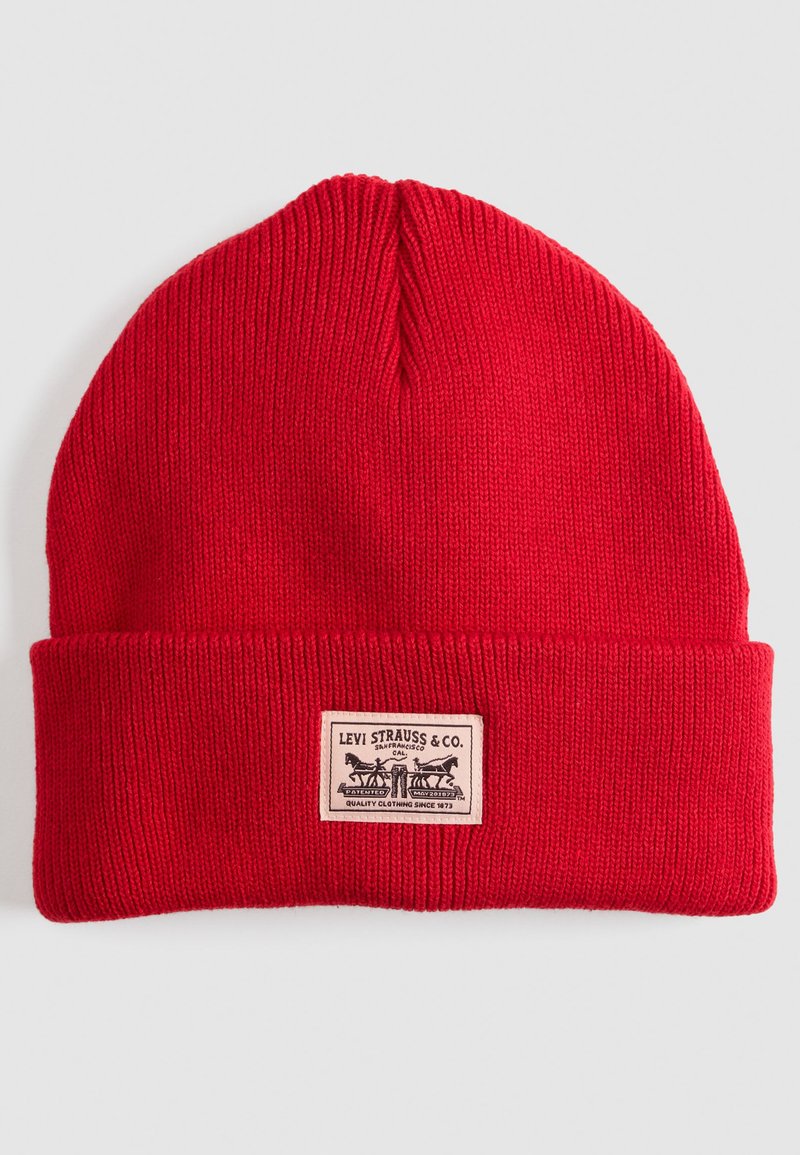 Rode gebreide beanie met ribbeltextuur en omgeslagen rand. Bevat een beige rechthoekig label met "Levi Strauss & Co." en grafisch ontwerp.