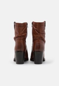 Para brązowych skórzanych butów do połowy łydki z blokowym obcasem, widziana od tyłu na jednolitym białym tle.