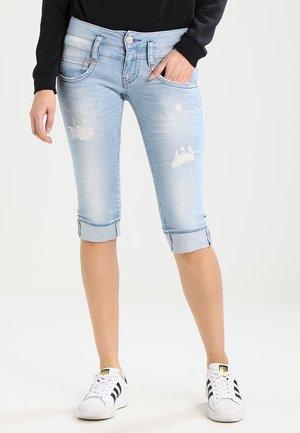 Pantalones cortos de denim azul claro desgastados hasta la rodilla con dobladillo remangado, usados con zapatillas blancas Adidas y camiseta negra de manga larga.