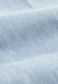 Gros plan sur un tissu en denim bleu clair montrant une texture tissée et un motif de tissage diagonal avec de légers plis.