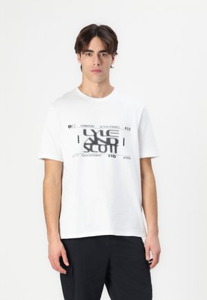 T-shirt en coton blanc à manches courtes, avec un design graphique noir comprenant du texte et des motifs géométriques sur le devant.