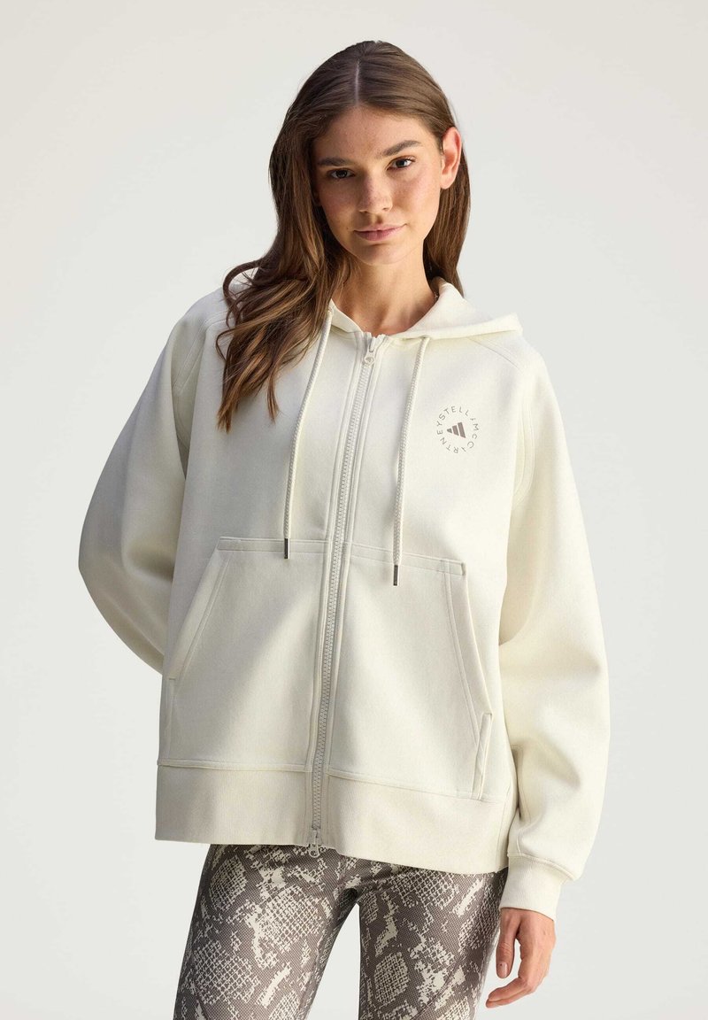 Felpa bianca con zip, logo frontale, grandi tasche e cappuccio con coulisse, abbinata a leggings grigio con motivo pitonato.