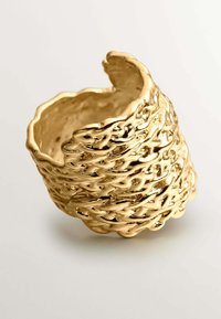 Anillo dorado con un diseño texturizado y retorcido. Presenta bordes irregulares y ondulados, además de un interior hueco. Superficie pulida y reflectante.
