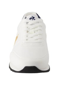 Sneaker bianco con tomaia in pelle liscia, punta tonda e lacci bianchi piatti. Presenta un logo in accento dorato e una suola nera in gomma.