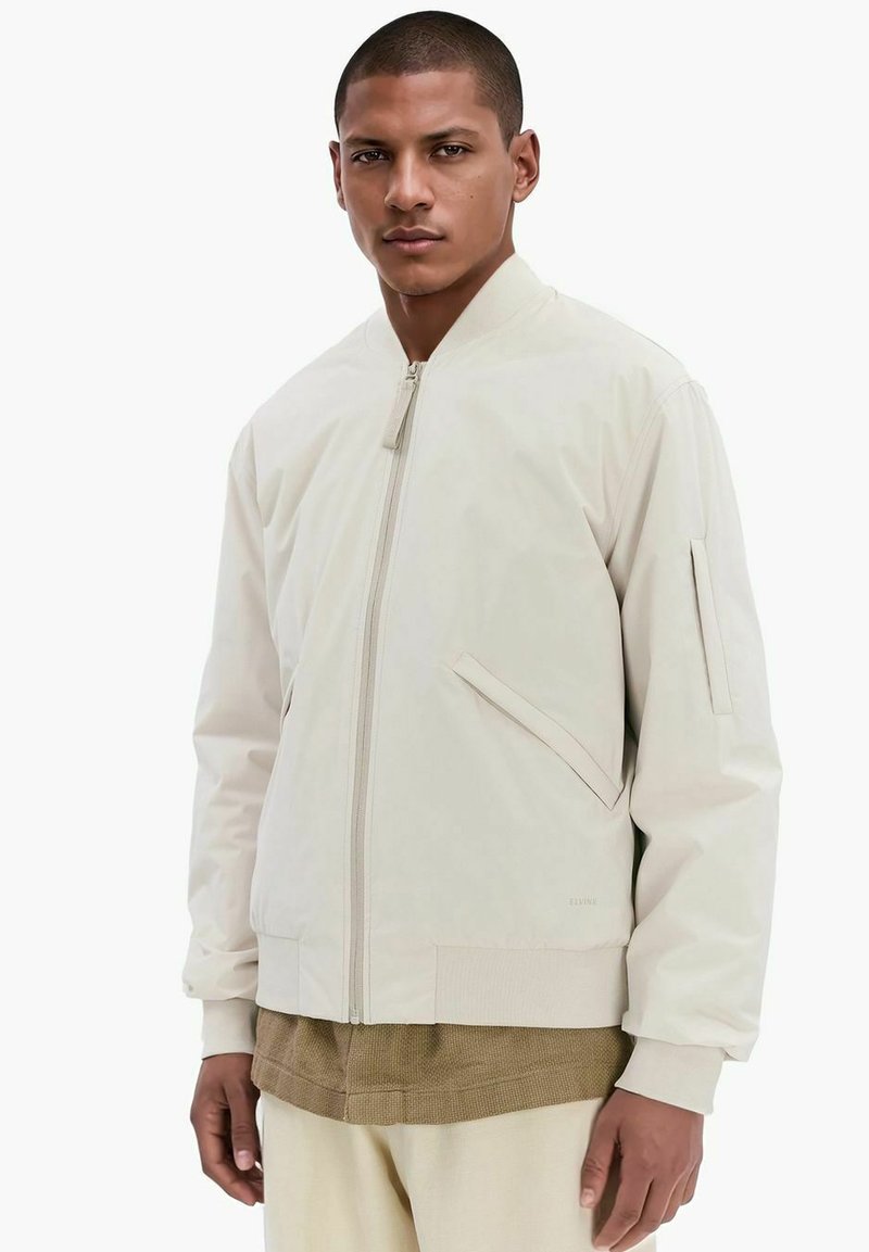 Lichtbeige bomberjack met een ritssluiting aan de voorkant, zij- en mouwzakken, ribgebreide manchetten en een gladde, matte textuur.