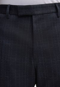 Navyblaue Hose mit einem strukturierten Muster, ausgestattet mit einem Bund und vorderen Falten. Hergestellt aus einem gewebten Stoff für ein formelles Erscheinungsbild.