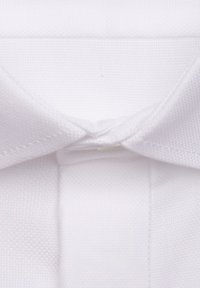 Camicetta bianca con colletto in tessuto textured con finitura liscia, che mostra dettagli di cucitura sul colletto e sulla pattina.