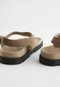 Zandalen van suede in lichtbruin met een zwarte rubberen zool, verstelbare band, platte hak en een zachte, gewatteerde inlegzool voor comfort.