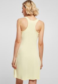 Vestido sin mangas de suave tela amarilla, con una forma ajustada y diseño de espalda nadadora. El dobladillo cae a medio muslo. Textura suave, con acentos mínimos.