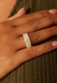 Silver and gold band ring with a row of small, clear rhinestones set in the center, placed on a textured green fabric.