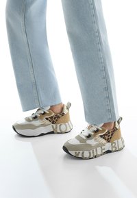 Sneakers with a leopard print design feature white, beige, and metallic gold accents, a chunky sole, and "VOILE BLEU" text on the side.