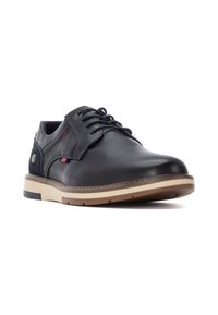 Zapato de cuero negro con una superficie lisa, puntera redonda, suela tan en contraste y costuras decorativas en acentos rojos y azules.
