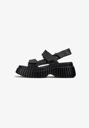 Black platform sandals featuring a chunky, ribbed sole, cut-out sections, and adjustable straps with textured accents for a secure fit.