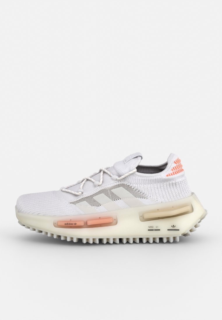 Zapatilla deportiva blanca con parte superior de punto, rayas grises y acentos en naranja. Cuenta con una suela gruesa y texturizada con inserciones de amortiguación de color.