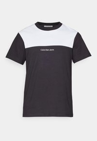 Camiseta de manga corta con un cuerpo negro y un panel superior blanco. Presenta el logo "Calvin Klein Jeans" en blanco en la parte frontal. Material de algodón.