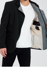 Czarna kurtka z sześcioma guzikami, dwoma przednimi kieszeniami i kieszenią na zamek. Wnętrze wyściełane szarą, paskowaną podszewką z wewnętrzną kieszenią.