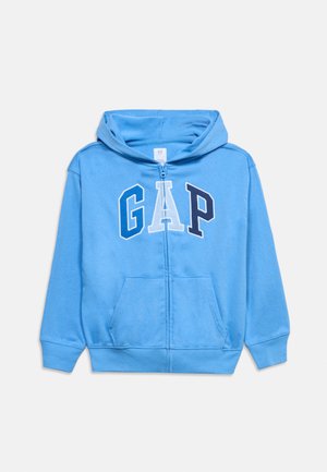 Lyseblå hættetrøje med lynlås, forrest kængurulomme og "GAP" bogstaver i blå, hvid og marineblå på brystet.