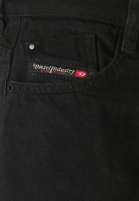 Mustekangas mustalla sävyllä, jossa on tasku punaisella ja harmaalla Diesel Industry -tunnuksella, joka osoittaa merkin ja farkkajaon.