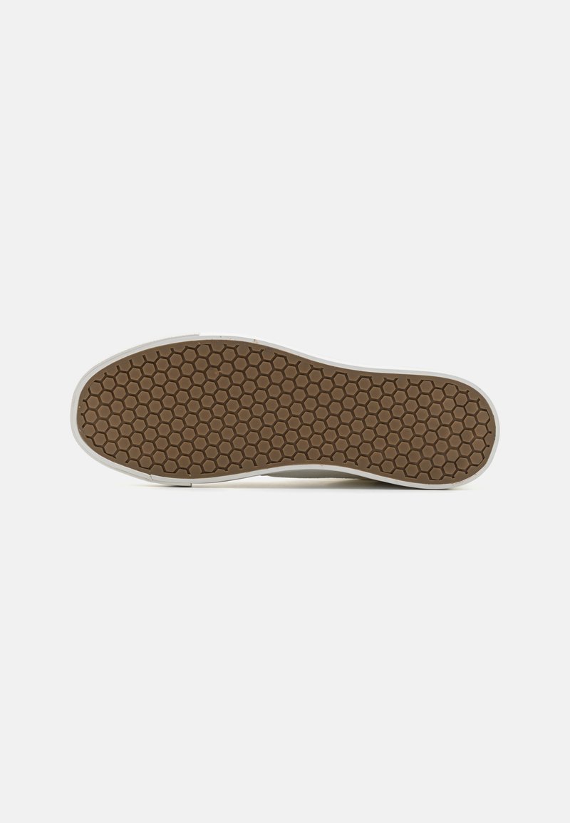 Semelle de chaussure avec un motif de crans hexagonaux bruns et une bordure blanche, vue par le dessous sur un fond blanc uni.