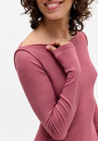 Langarm, getailleerd shirt in zachte mauve stof met een bootnek en subtiele plooidetails op de mouwen, dat een gladde textuur toont.