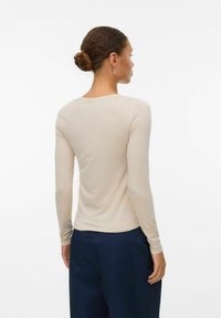 Ljus beige långärmad topp med rundad halsringning och ribbad textur, kombinerad med marinblå byxor. Bakifrån visas åtsittande ärmar och midja.