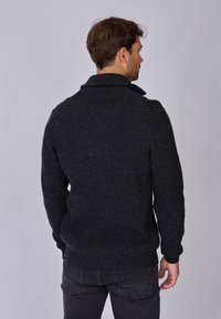 Pull en maille gris foncé avec un col montant et une texture côtelée, présentant de longues manches et un bas ajusté. Vue de dos affichée.