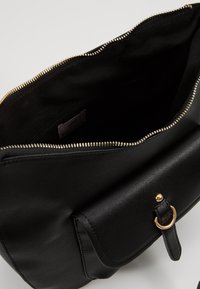 Borsa in pelle nera con una cerniera dorata, dotata di una morbida fodera interna, una patta frontale con un'impronta a forma di anello e un design elegante.