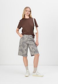 Brun t-skjorte, løstsittende shorts med leopardmønster, hvit håndveske, beige sokker og hvite joggesko. Glatt stoff, uformell design, lengde til midten av låret.
