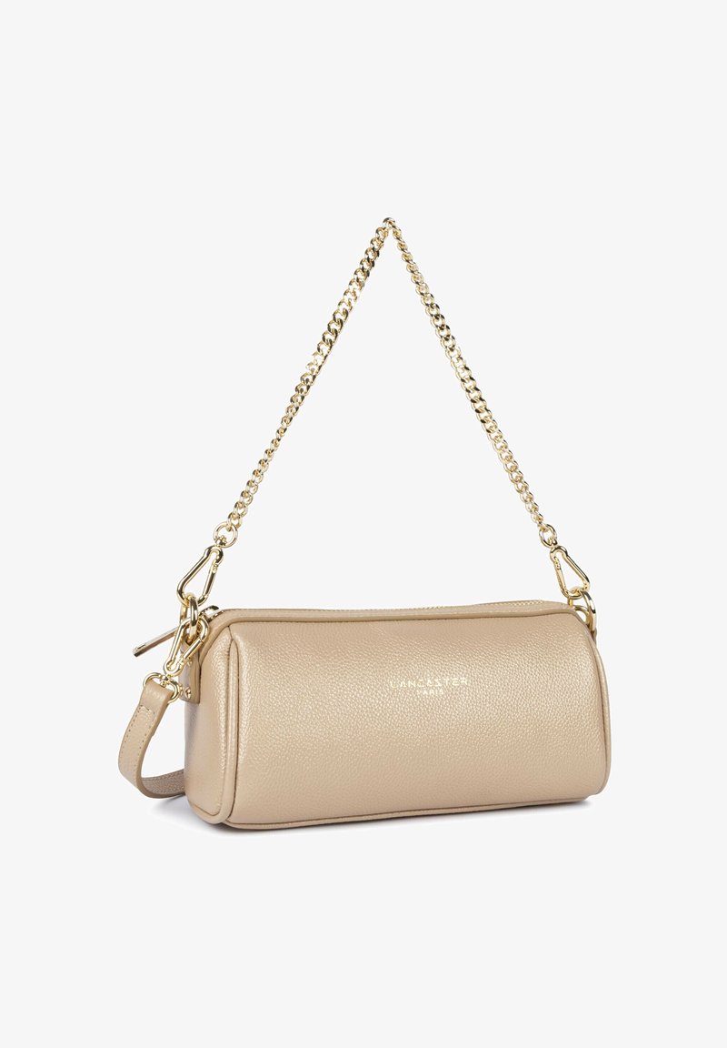 Sac à main cylindrique en cuir texturé beige avec bandoulière chaîne dorée et fermeture éclair, marqué « LANCASTER PARIS » à l'avant.