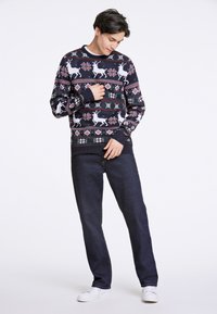 Suéter azul-marinho com padrões de renas brancas e florais, com punhos e gola canelados, combinado com jeans escuros e ténis brancos.