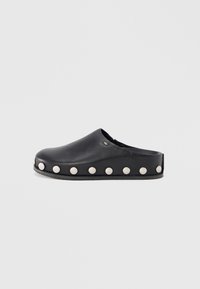 Black leather clog with a rounded toe and flat sole, featuring raised white studs along the sides for accent detail.