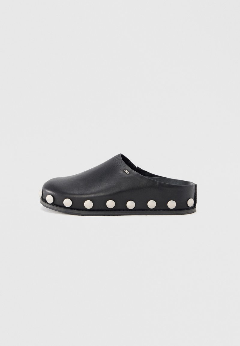 Black leather clog with a rounded toe and flat sole, featuring raised white studs along the sides for accent detail.
