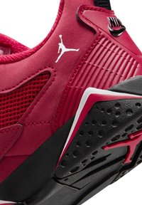 Sneaker sintetico rosso con dettagli in rete, logo bianco, pannello laterale testurizzato e suola in gomma nera con superficie a grip modellata.