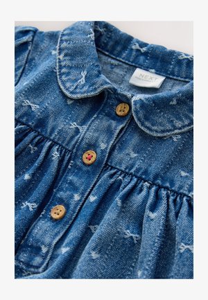 Sukienka dżinsowa z niebieskiej tkaniny, z kołnierzykiem i zapięciem na guziki. Charakteryzuje się marszczoną fakturą i rozproszonymi białymi wzorami. Guziki mają naturalny, drewniany kolor.