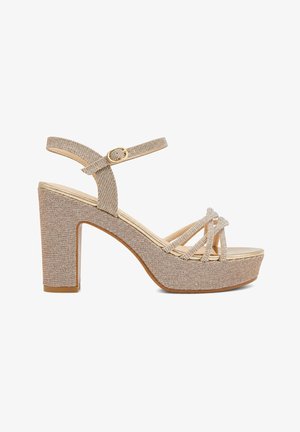 Sandalia plataforma beige con brillo, tacón ancho, tiras cruzadas sobre los dedos y correa ajustable en el tobillo con hebilla dorada.
