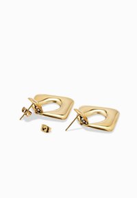 Naušnice u obliku kvadrata u zlatnoj boji s šupljim središtem i glatkim, zaobljenim rubovima. Imaju kopču s čepom i leptirasti zatvarač. Uključuju dodatnu pozadinu.