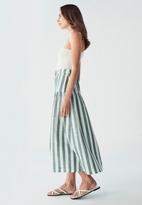 Pruhovaná maxi sukňa s vertikálnymi zelenými a bielymi pruhmi, vyrobená z ľahkej tkaniny. Kombinovaná s priliehavým bielym topom a plochými sandálmi.