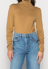 Un pull col roulé marron en matière douce et légère avec des manches longues ajustées, associé à un jean en denim bleu taille haute.