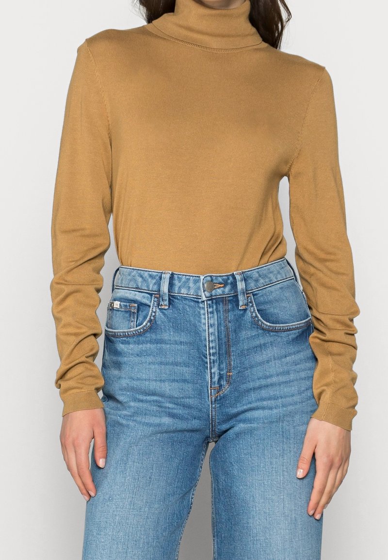 Un pull col roulé marron en matière douce et légère avec des manches longues ajustées, associé à un jean en denim bleu taille haute.