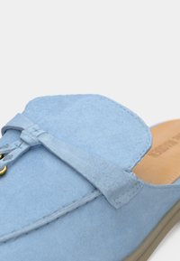 Γαλάζιο σουεντ παπούτσι τύπου slip-on με στρογγυλεμένη μύτη, διακοσμητικό φιόγκο, και χρυσούς μεταλλικούς κρίκους, με διακριτική υφή και ραμμένες λεπτομέρειες.