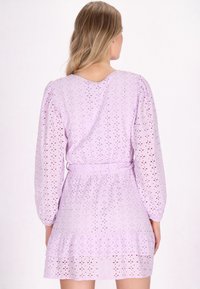 Lawendowa sukienka z dopasowanym wąskim wcięciem w talii, bufkami oraz warstwową spódnicą. Materiał zdobiony jest detalami typu eyelet, co dodaje tekstury.