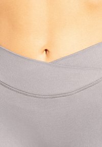 Top sportivo grigio chiaro con una scollatura ampia e a costine e un design senza cuciture, che enfatizza una texture liscia e uno stile minimalista.