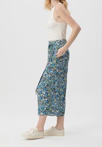 Blommigt tryck, kjol i midjelängd i blå, grön och vit nyanser, tillverkad av lättviktsmaterial med elastisk midja och sidofickor. Kombinerad med vita sneakers.