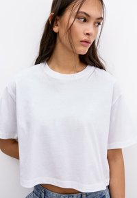 Tricou alb scurt, confecționat din bumbac moale, cu decolteu rotund �și mâneci scurte, având o croială lejeră. Textură netedă, design minimalist.