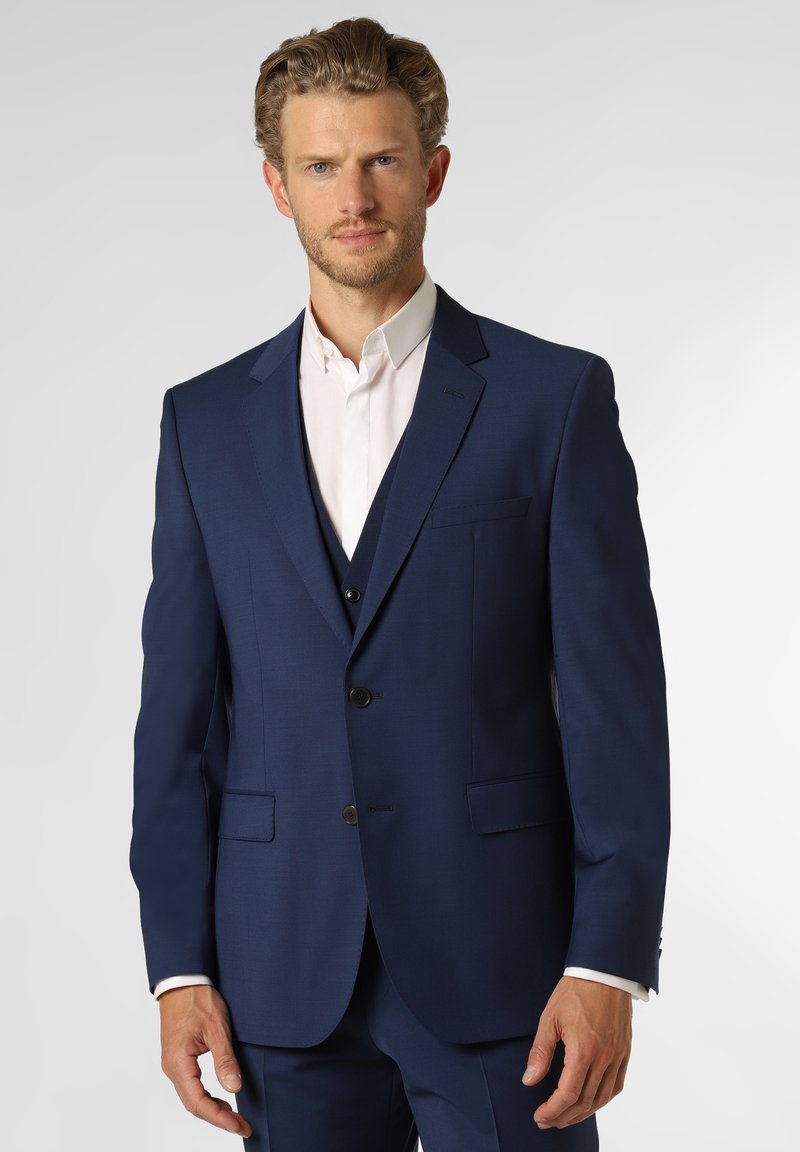 Completo su misura blu navy con design a un bottone, rever a punta e due tasche frontali. Indossato sopra una camicia bianca.