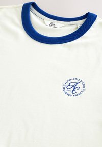 Biały T-shirt z niebieskim prążkowanym kołnierzem, z nadrukowanym okrągłym logo w kolorze niebieskim z napisem "ALPES-CÔTE D'AZUR PROVENCE - FRANCE".