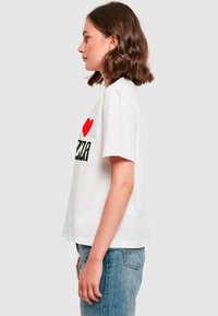 T-shirt en coton blanc à manches courtes. L'avant présente un graphique rouge et noir "J ❤️ PIZZA". Coupe ample, longueur hip, texture douce.