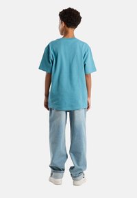 Turkoosi puuvillainen T-paita lyhyillä hihoilla, yhdistettynä vaaleansinisiin farkkuihin. Pehmeä materiaali, rento malli ja yksinkertainen muotoilu.