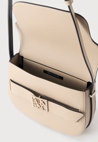 Μπεζ τσάντα χιαστί με ανοιχτό καπάκι, μπροστινή τσέπη και λογότυπο Armani Exchange στον κούμπωμα· ρυθμιζόμενο λουράκι με ασημένια λεπτομέρεια αγκράφας.