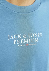 Gaiši zils kokvilnas T-krekls ar apaļu apkakli un baltu logo tekstu "JACK & JONES PREMIUM" ar reģistrētas preču zīmes simbolu.